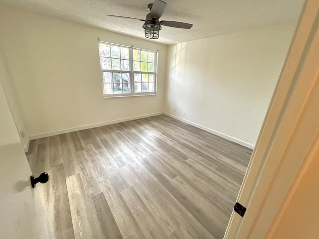 empty room with light wood-style floors, baseboards, and a textured ceiling