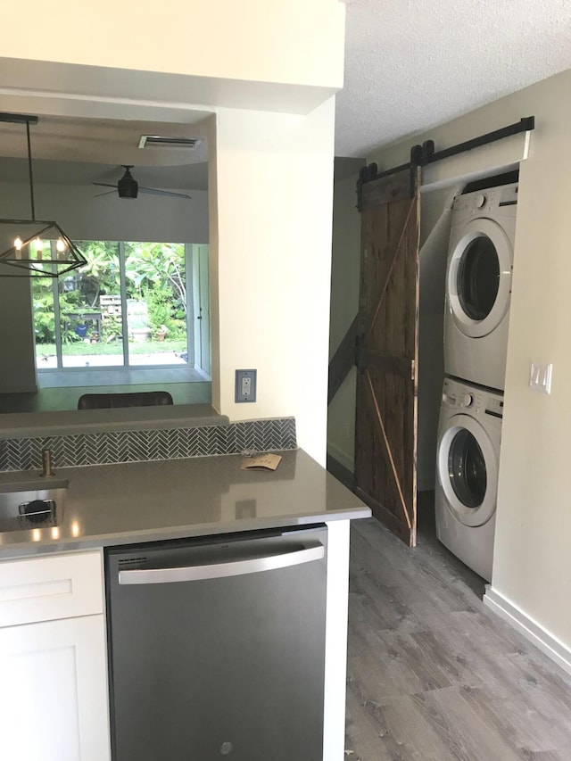 laundry room featuring a barn door, visible vents, wood finished floors, a textured ceiling, and stacked washing maching and dryer