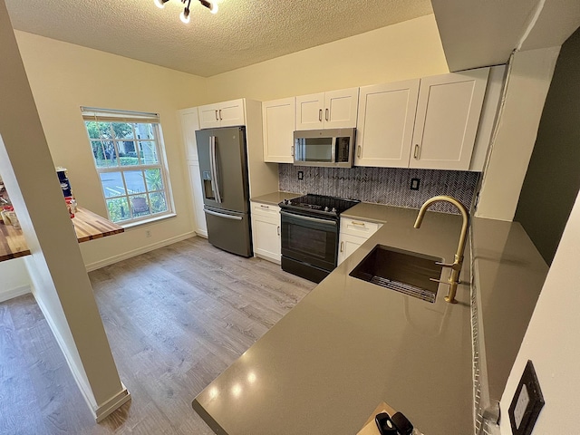 kitchen with stainless steel appliances, light wood-style flooring, white cabinets, a sink, and a textured ceiling