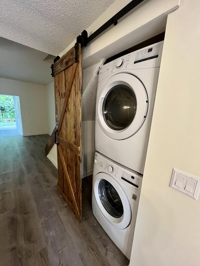 laundry room featuring a textured ceiling, a barn door, stacked washer and dryer, laundry area, and wood finished floors