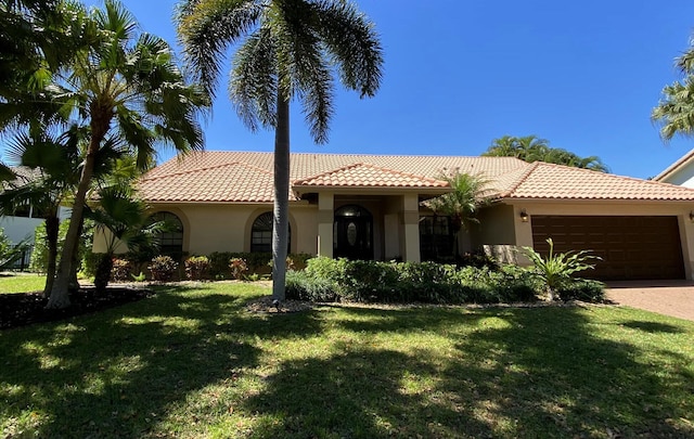 mediterranean / spanish home with a garage, a tile roof, a front lawn, and stucco siding