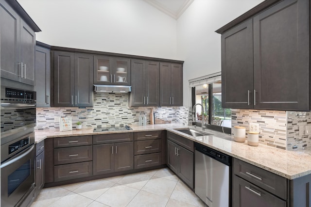 kitchen with ornamental molding, a sink, light stone counters, under cabinet range hood, and appliances with stainless steel finishes