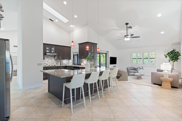 kitchen with a breakfast bar area, light stone counters, light tile patterned flooring, freestanding refrigerator, and open floor plan
