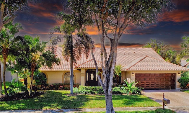 view of front of property with a tiled roof, an attached garage, a lawn, and stucco siding