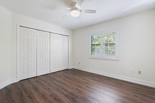 unfurnished bedroom with a closet, a ceiling fan, dark wood-type flooring, and baseboards
