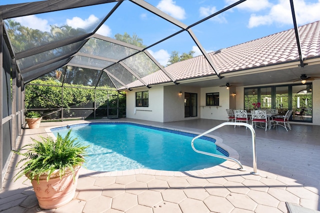 outdoor pool with glass enclosure, a patio, and a ceiling fan