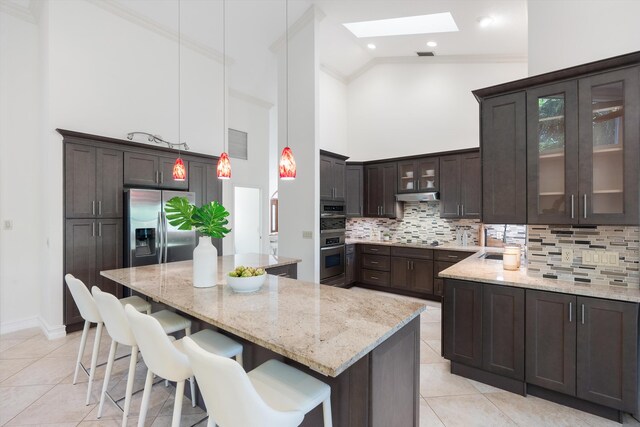 kitchen featuring under cabinet range hood, a center island, stainless steel appliances, light tile patterned floors, and dark brown cabinets
