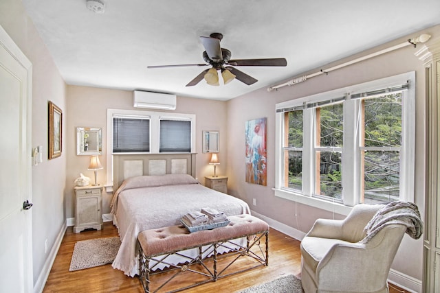 bedroom with ceiling fan, baseboards, wood finished floors, and a wall mounted AC