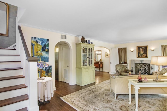 living room with visible vents, arched walkways, dark wood-style flooring, stairs, and crown molding