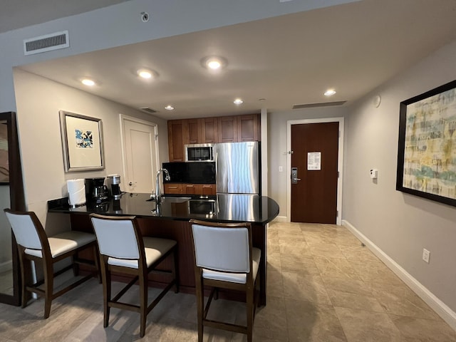 kitchen with dark countertops, visible vents, a kitchen bar, appliances with stainless steel finishes, and a peninsula