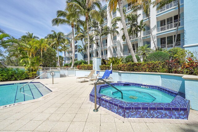 pool with a patio area, fence, and a hot tub