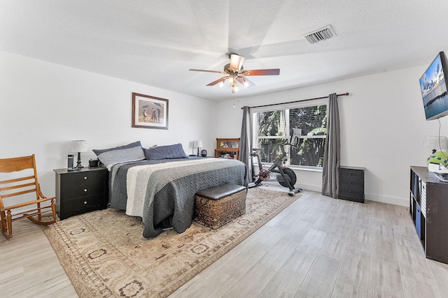 bedroom with light wood finished floors, visible vents, a textured ceiling, and baseboards