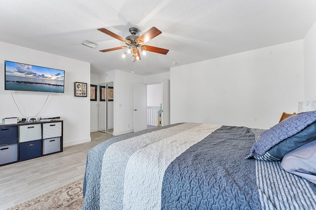 bedroom with baseboards, visible vents, light wood finished floors, ceiling fan, and a textured ceiling