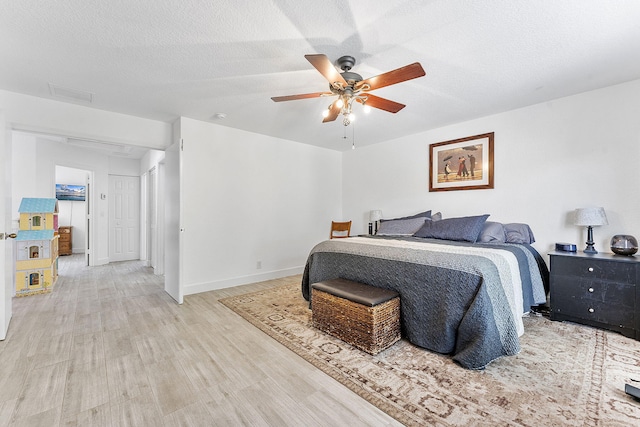 bedroom featuring visible vents, a textured ceiling, light wood finished floors, baseboards, and ceiling fan