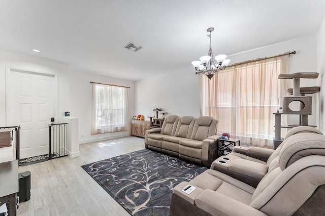 living area featuring baseboards, visible vents, light wood-style flooring, a textured ceiling, and a notable chandelier