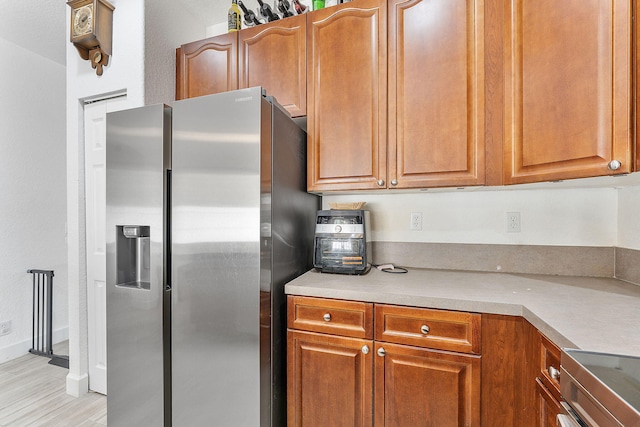 kitchen featuring brown cabinetry, stainless steel fridge, light countertops, and baseboards