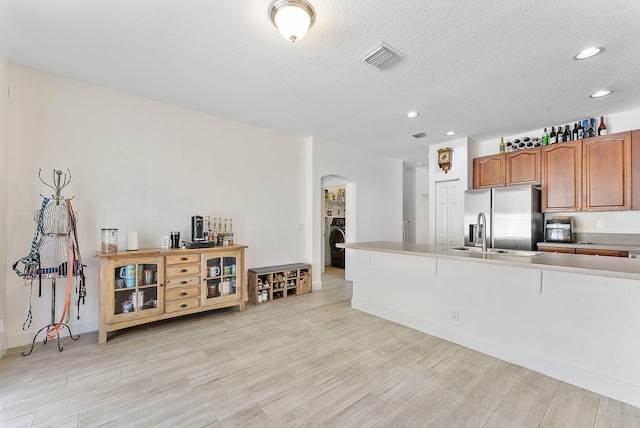 kitchen with visible vents, brown cabinets, stainless steel refrigerator with ice dispenser, a sink, and arched walkways