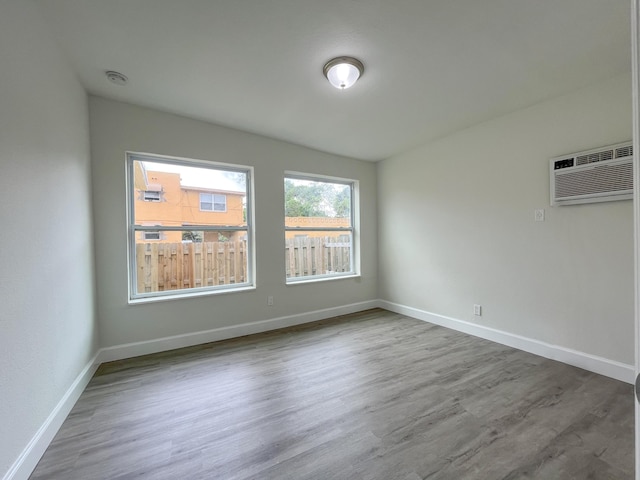 unfurnished room with baseboards, wood finished floors, and a wall mounted air conditioner