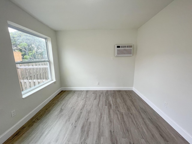 empty room featuring a wall mounted air conditioner, baseboards, and wood finished floors