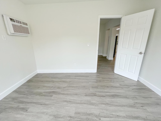 unfurnished room featuring light wood-type flooring, baseboards, and a wall mounted AC