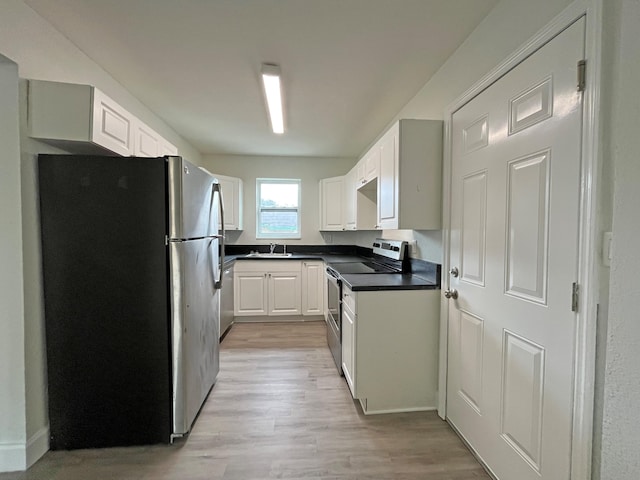 kitchen featuring a sink, white cabinetry, appliances with stainless steel finishes, light wood finished floors, and dark countertops