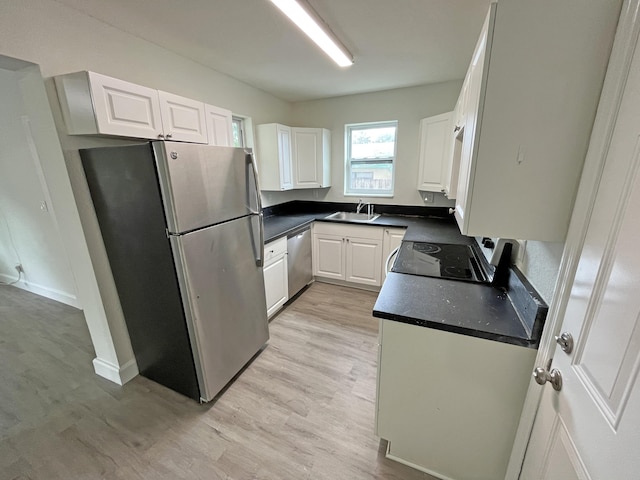 kitchen with light wood finished floors, dark countertops, appliances with stainless steel finishes, white cabinetry, and a sink