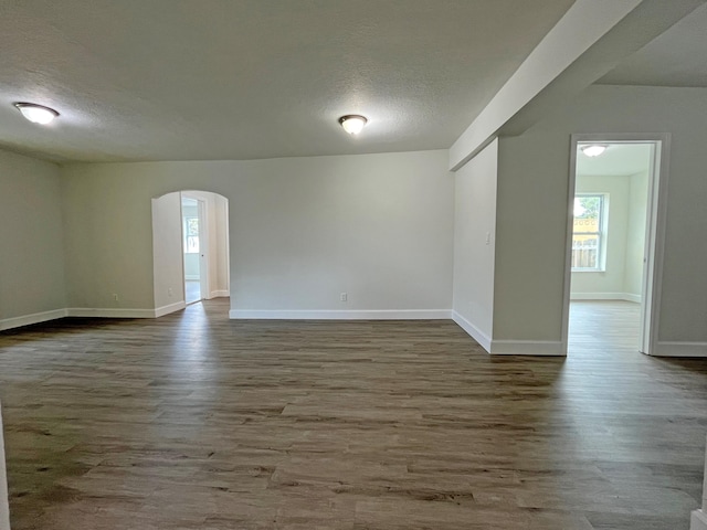 unfurnished room with baseboards, a textured ceiling, arched walkways, and wood finished floors