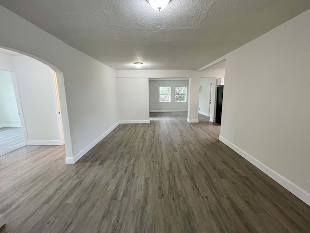 spare room featuring dark wood-style floors, baseboards, arched walkways, and a textured ceiling