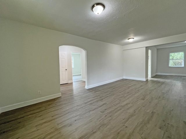 empty room with baseboards, a textured ceiling, arched walkways, and wood finished floors