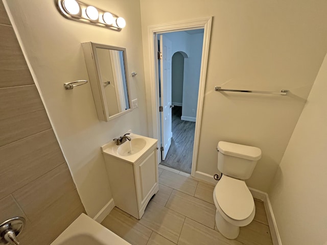 full bathroom featuring toilet, a bathing tub, baseboards, and vanity