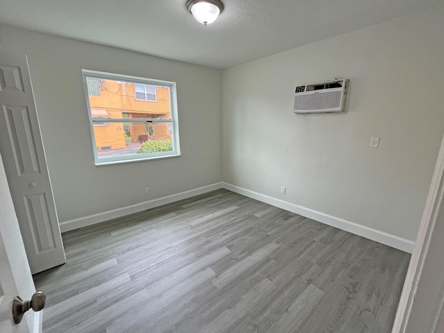 unfurnished bedroom with a wall mounted air conditioner, wood finished floors, and baseboards