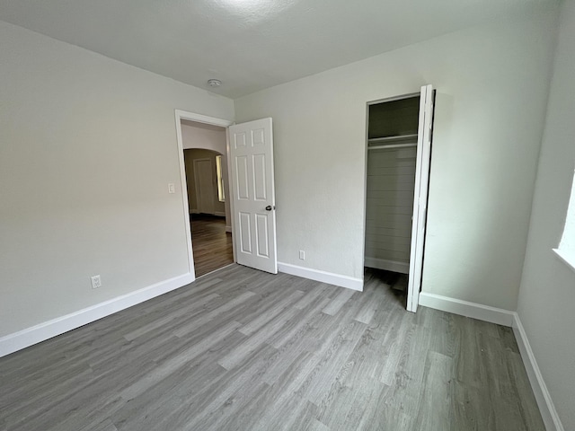 unfurnished bedroom featuring arched walkways, a closet, wood finished floors, and baseboards