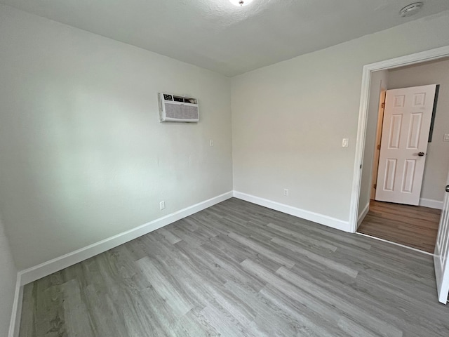 unfurnished room featuring wood finished floors, baseboards, and a wall mounted AC