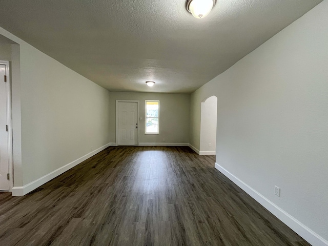 interior space with arched walkways, a textured ceiling, dark wood-style floors, and baseboards