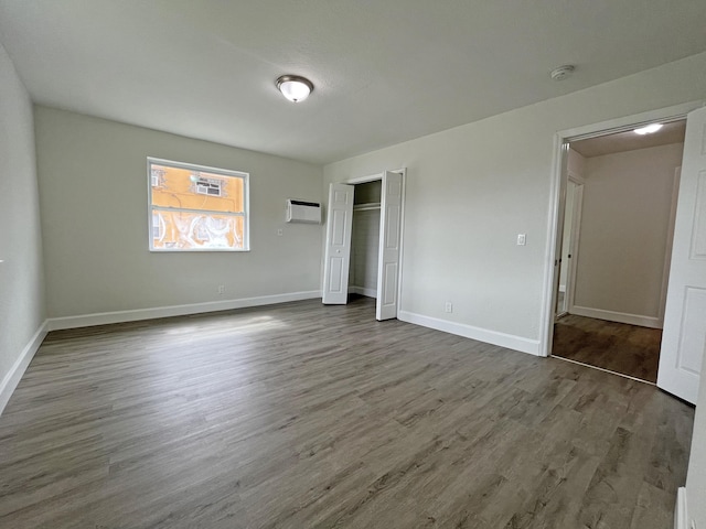 unfurnished bedroom with dark wood-style floors, a closet, a wall unit AC, and baseboards