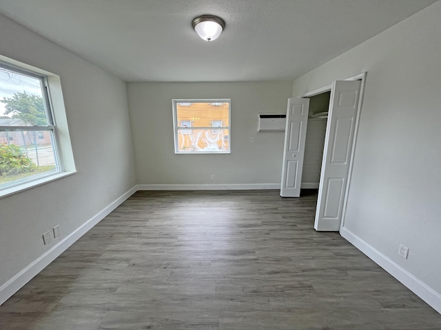 unfurnished bedroom featuring a closet, a wall mounted air conditioner, dark wood finished floors, and baseboards