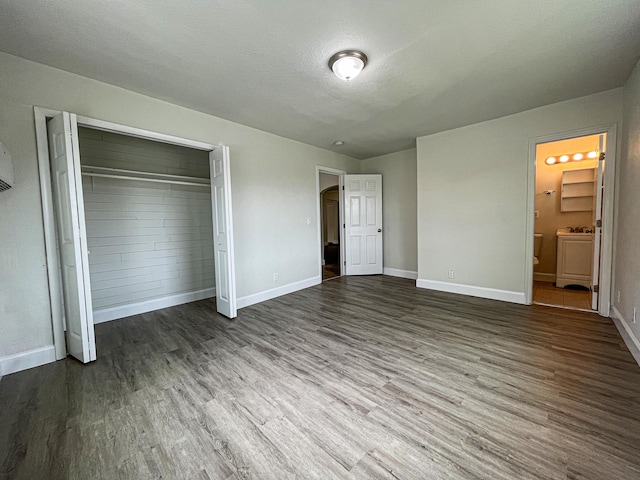 unfurnished bedroom with a closet, ensuite bathroom, a textured ceiling, wood finished floors, and baseboards