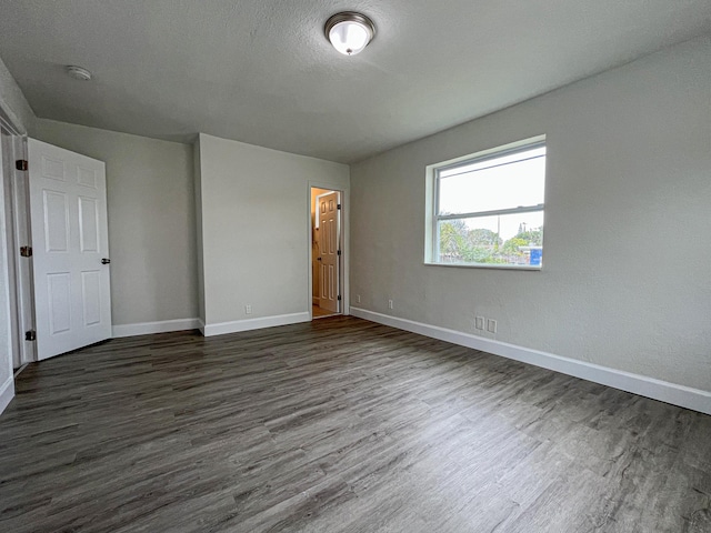 unfurnished room with a textured ceiling, baseboards, and dark wood-type flooring