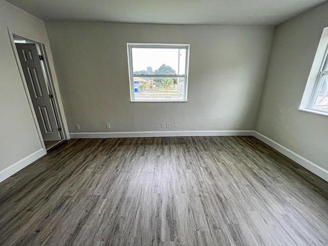 empty room featuring dark wood-style floors, a wealth of natural light, and baseboards