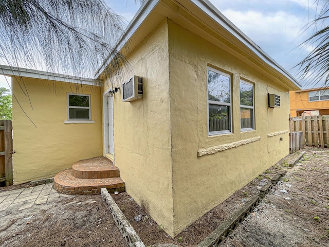 view of side of home featuring a wall mounted air conditioner, fence, and stucco siding