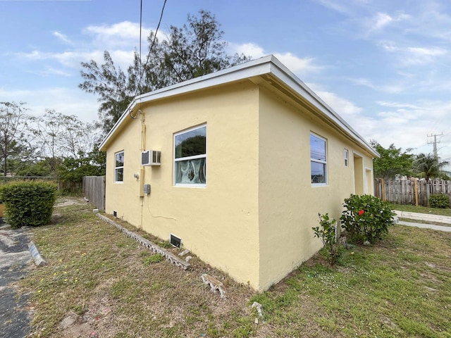 view of property exterior with a lawn, a wall mounted air conditioner, fence, and stucco siding