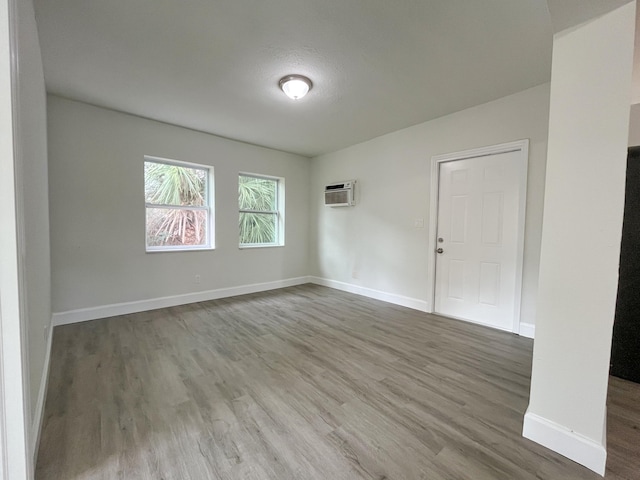 unfurnished room featuring a wall unit AC, wood finished floors, and baseboards