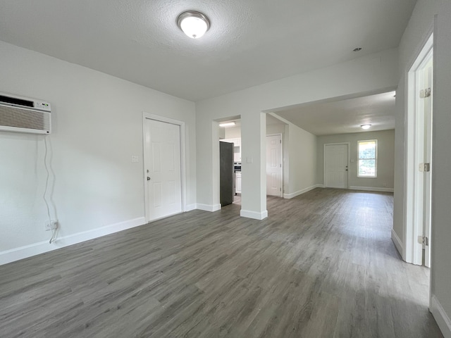 interior space with an AC wall unit, a textured ceiling, baseboards, and wood finished floors