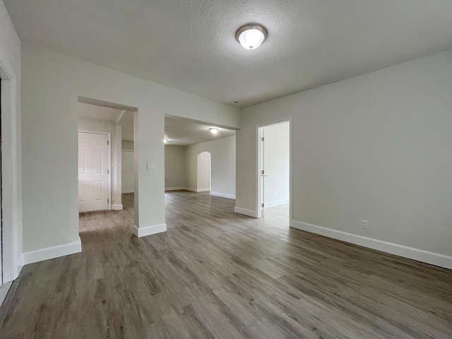 empty room featuring arched walkways, a textured ceiling, baseboards, and wood finished floors