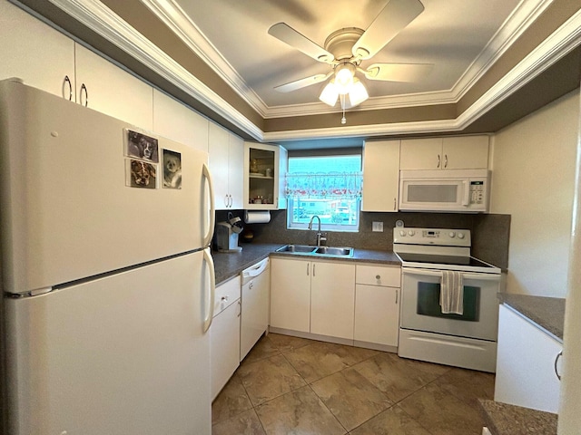 kitchen with white appliances, a raised ceiling, dark countertops, ornamental molding, and a sink