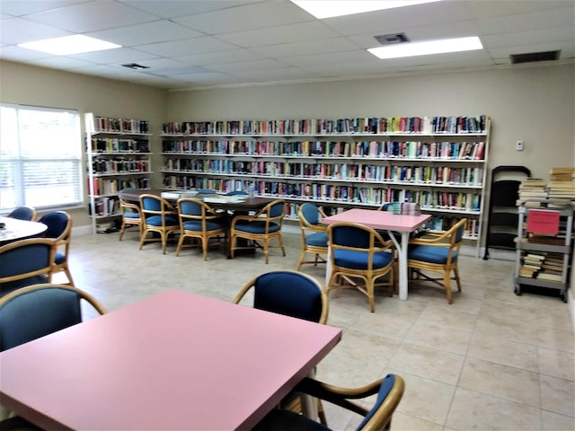 interior space featuring a paneled ceiling, tile patterned flooring, visible vents, and wall of books