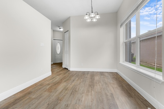 unfurnished dining area with an inviting chandelier, wood finished floors, and baseboards