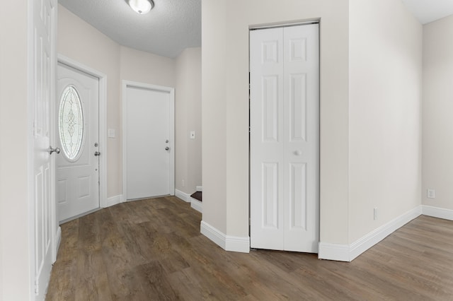 foyer entrance with a textured ceiling, baseboards, and wood finished floors