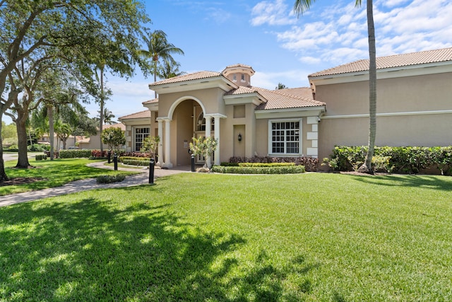 mediterranean / spanish-style home featuring a front yard, a tiled roof, and stucco siding