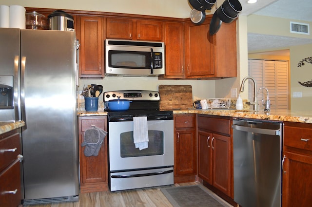 kitchen with visible vents, a sink, light wood-style floors, appliances with stainless steel finishes, and light stone countertops